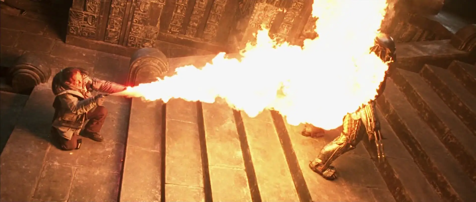 A human fires a stream of flame down a stone stair toward a Predator.