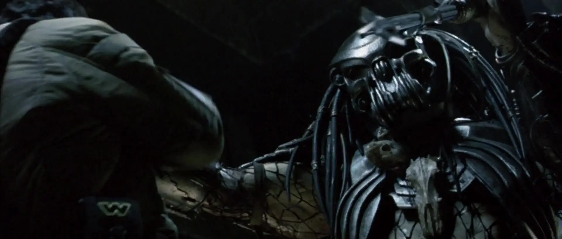 Predator grapples a trapped human in dim blue light.